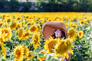 Teenage girl in hat and sunglasses having fun in the field of sunflowers