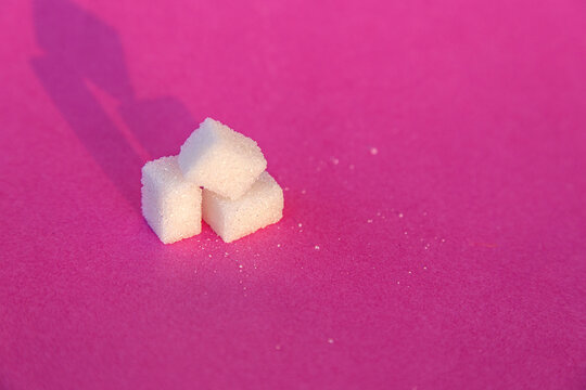 Three cubes of white shugar on the pink background