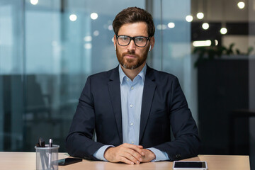 Portrait of a mature boss in a business suit, a businessman is sitting at a desk and looking at the...