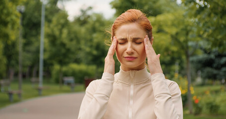 Female having a headache while jogging. Woman stops running because a head pain. Severe migraine concept. Emotions of strong suffering. Pills prescription, fitness training health problems.