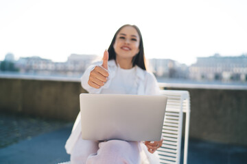 Positive woman using laptop and showing thumb up in city