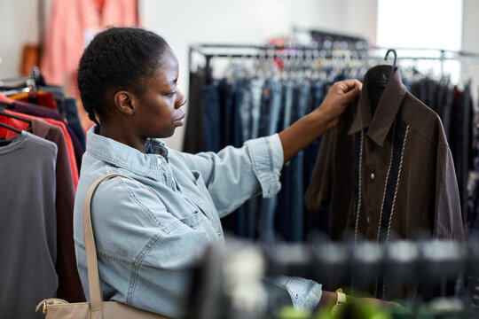 Side view portrait of black young woman looking at clothes in second hand store