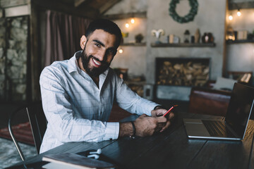 Smiling ethnic man working on laptop and browsing mobile