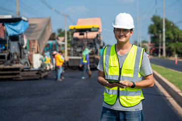 Asian handsome civil engineer under inspection and survey workplace by tablet with Asphalt paver &...