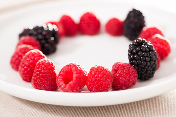 raspberries and blackberries laid out on a white plate in circle