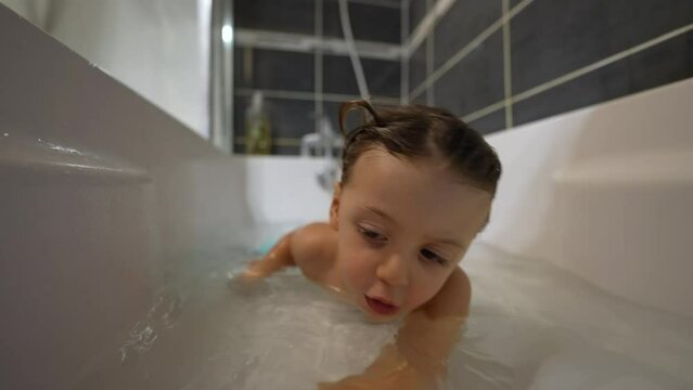 One little boy playing at bathtub with toy boat. Playful child bathing inside tub