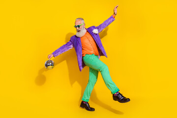 Fototapeta na wymiar Full length photo of charming positive guy dressed violet velvet jacket having fun holding disco ball hands sides isolated yellow color background