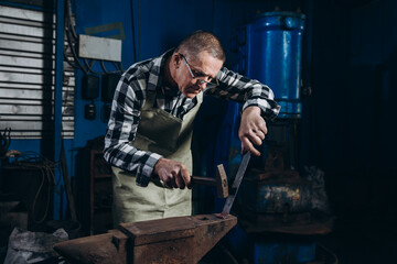 Senior an artisan blacksmith knocks with a hammer on iron to shape 