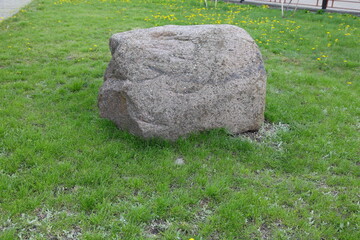 A huge boulder-stone lies in the park on the green grass.