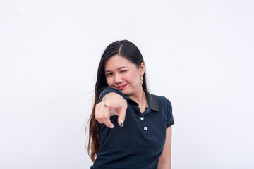A young asian woman points directly in front while winking. Endorsing or singling out someone. Isolated on a white background.