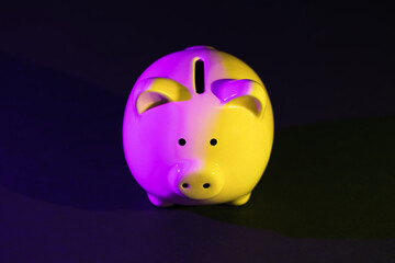 Piggy bank on a dark background with violet-yellow backlight. Banking concept. Bright neon lights on a black background