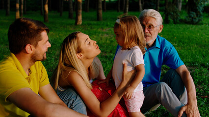 Fototapeta premium Pretty little girl and her parents together with grandfather have a lovely family time together in the middle of the park they enjoy the time together