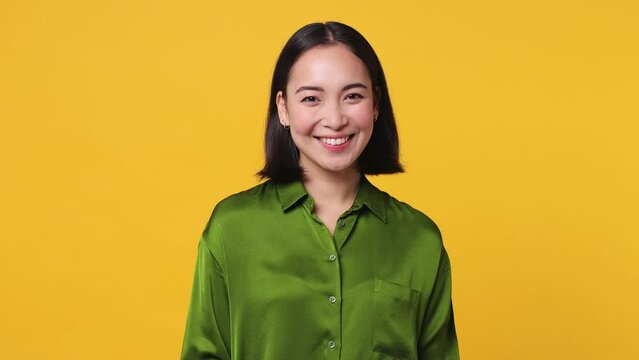 Beautiful charming happy fun young woman of Asian ethnicity 20s she wear green shirt posing looking camera smiling with sincere emotion isolated on plain yellow color wall background studio portrait