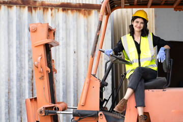 Female foreman wears hard hat driving forklift at shipping container yard, portrait. Multiracial industrial engineer woman drives reach stacker truck to lift cargo box at logistic terminal dock.