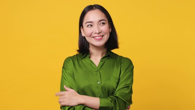 Beautiful young woman of Asian ethnicity 20s she wear green shirt look around think dream put hand prop up on chin lost in thought and conjectures isolated on plain yellow color wall background studio