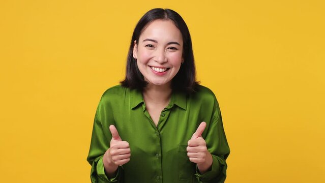 Back rear view beautiful young woman of Asian ethnicity 20s she wear green shirt turn around camera showing thumbs up sign like gesture isolated on plain yellow color wall background studio portrait