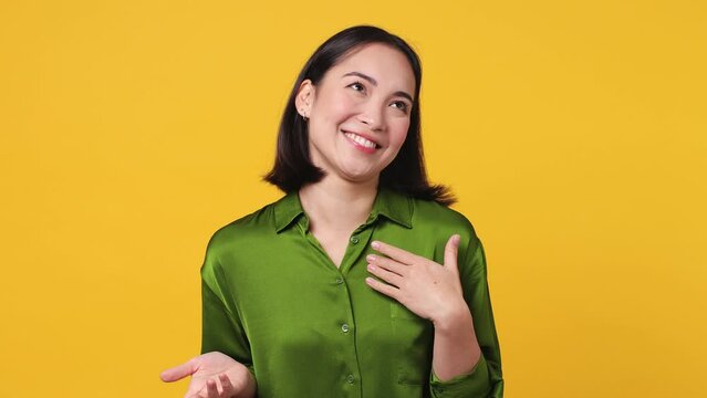 Beautiful portrait young woman of Asian ethnicity 20s she wear green shirt look camera pointing fingers herself ask say who me no thanks i do not need it isolated on plain yellow color wall background