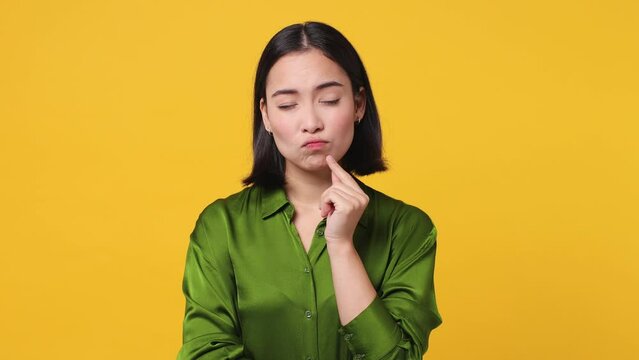 Puzzled young woman wear green shirt look aside put hand prop up on chin iterates over solution options feel doubtful thinks but no decision comes isolated on plain yellow color wall background studio