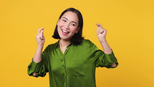 Beautiful young woman 20s she wear green shirt dance waving expressive gesticulating hands fool around have fun enjoy snaps her fingers to music rhythm isolated on plain yellow color wall background