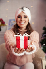 Obraz na płótnie Canvas Woman holding a Christmas present. Beautiful cheerful woman gives a red gift against a background of Christmas tree. New Year and Christmas concept. Merry Christmas and happy holidays
