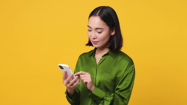 Young happy woman 20s she wear green shirt hold use mobile cell phone swipe send sms doing online shopping order delivery to home booking tour isolated on plain yellow color background studio portrait
