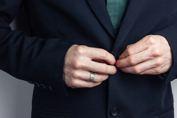 Obraz premium Male hands of a businessman in a business suit with a ring on his finger fasten a button on a jacket. Horizontal orientation photo, business style.
