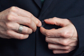 Male hands of a businessman in a business suit with a ring on his finger fasten a button on a...