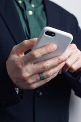 Male hands of a businessman in a business suit with a ring on his finger hold a modern gadget, a phone in a white case in his hands. Vertical orientation photo, business style.
