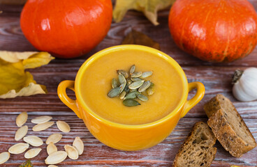 Seasonal food. Pumpkin cream soup and homemade rye bread on a wooden table. Close-up. Selective focus.