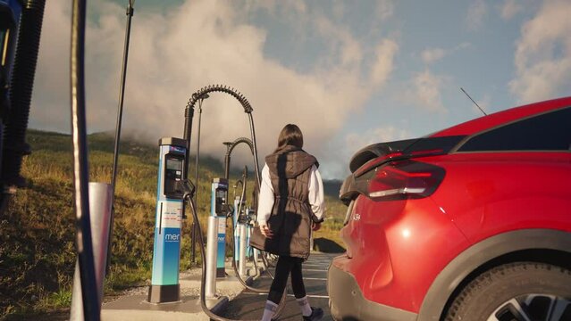 A woman charging a red electric vehicle