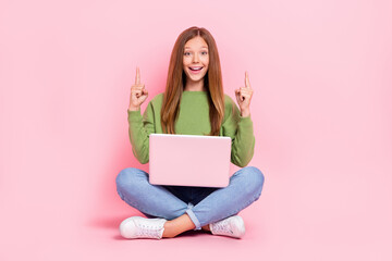 Full length photo of cute excited school girl dressed sweatshirt pointing empty space working modern device isolated pink color background