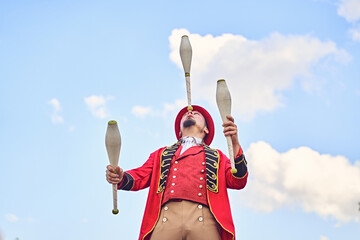 From below man in red costume balancing club on nose while juggling against cloudy blue sky during...