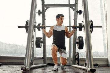 Fototapeta premium sport, bodybuilding, lifestyle and people concept - young man with barbell flexing muscles and making shoulder press lunge in gym