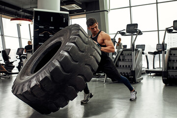 Muscular fitness man moving large tire in gym center, concept lifting, workout training.