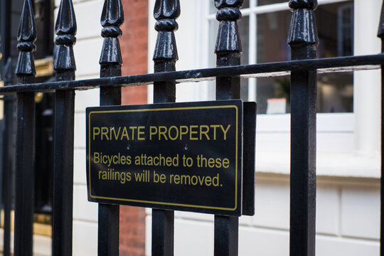 A "Private Property" sign on a city street. Black metal warning sign on public fence "Private property - Bicycles attached to these railings will be removed."