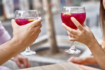 Crop anonymous couple in love clinking glasses with red refreshing cocktails while celebrating anniversary in street cafe in summer
