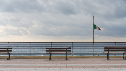 Benches on the promenade of Varazze, Liguria, Italy, on the coastline of mediterranean sea. It is a typical vacation village. Dramatic sky on the background.