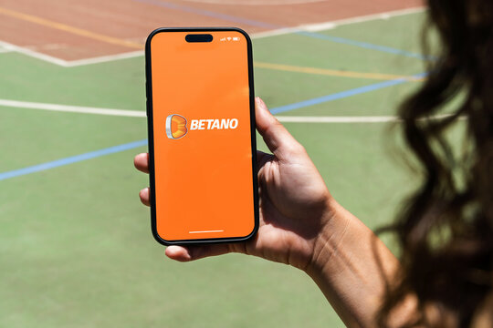 Girl holding an iPhone 14 Pro smartphone with Betano betting provider app on screen. Multi-sport court in the background. Rio de Janeiro, RJ, Brazil. November 2022