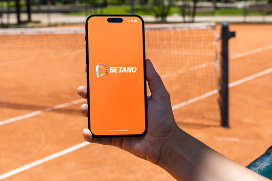Girl holding an iPhone 14 Pro smartphone with Betano betting provider app on screen. Clay tennis court in the background. Rio de Janeiro, RJ, Brazil. November 2022