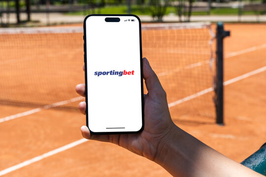 Girl holding an iPhone 14 Pro smartphone with Sportingbet betting provider app on screen. Clay tennis court in the background. Rio de Janeiro, RJ, Brazil. November 2022