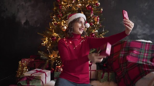 White woman in red sweater holds smart phone make video call on Christmas Eve 