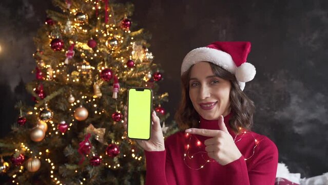 Woman in red sweater and Santa's hat holding a mobile phone with a green screen