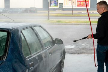 Car wash or cleaning with high pressure water using foam. Hand washing the car with water.  A man washes his car at a self-service car wash.