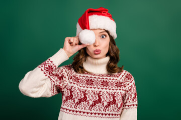 Photo of charming lady pouted lips kiss arm hold headwear pompom ball cover eye isolated on green color background