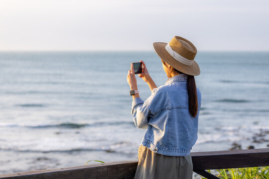 Travel woman use cellphone to take photo at seaside under sunset period