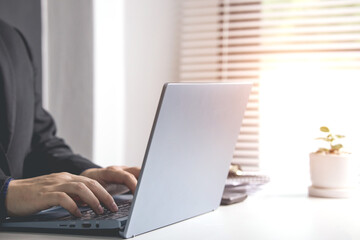 Businessman or accountant typing keyboard on laptop computer with business documents on office table with blurred window background. concept of document work Connecting internet network technology