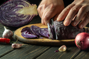 The hands of the chef are cutting red cabbage with a knife on a kitchen cutting board. Cooking...