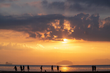 Naklejka na ściany i meble tourist watching sunset or sunrise on beach with seascape and gold lighting sunset sky background