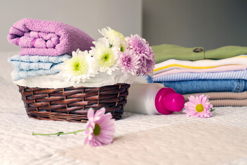 Stack of clean, colorful clothes and flowers on the bed