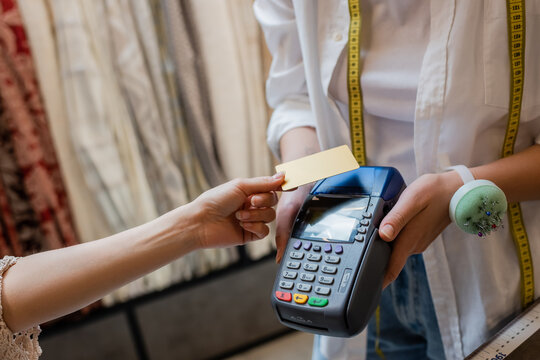 cropped view of saleswoman holding credit card reader near client in textile shop